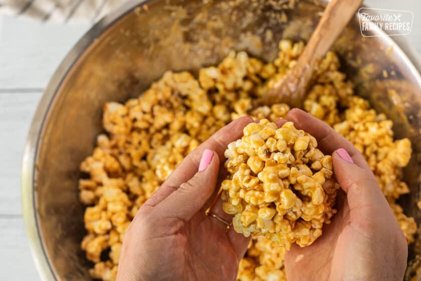 Rolling a ball of caramel popcorn with hands over a bowl of caramel popcorn.