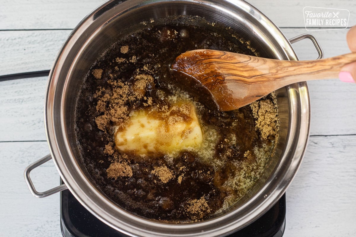 Wooden spoon stirring brown sugar, corn syrup and butter in a saucepan.