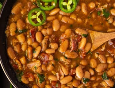 Charro Beans in a bowl with a wooden spoon and garnished with sliced jalapeños.