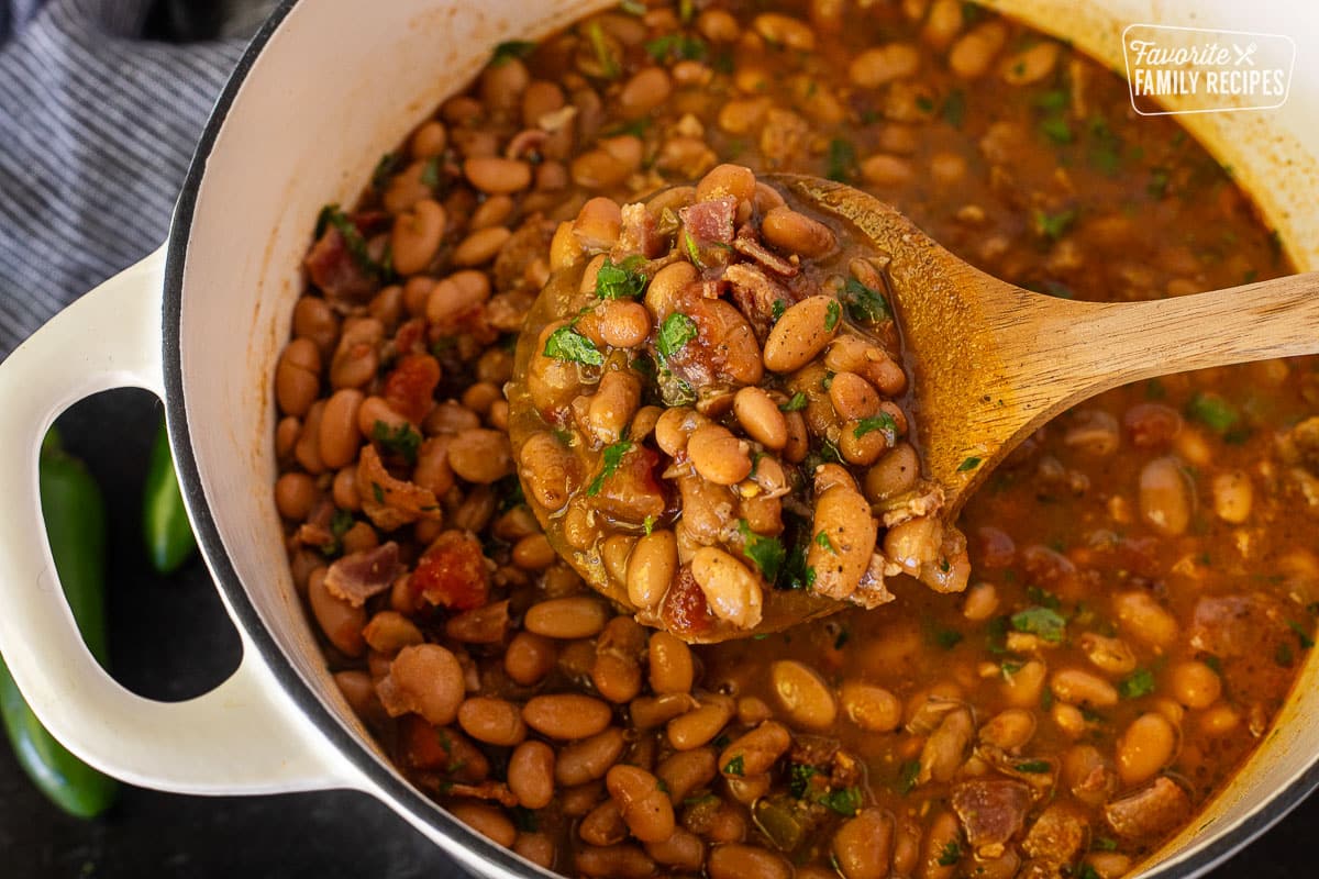 Spoon holding up Charro Beans over a dutch oven.