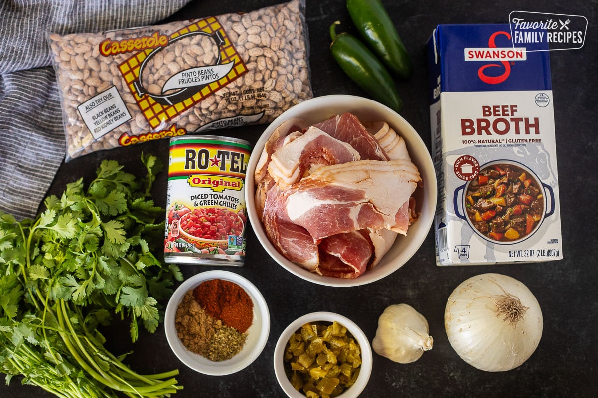 Ingredients to make Charro Beans including pinto beans, beef broth, jalapeños, bacon, rotten, spices, jalapeños, cilantro, garlic and onion.