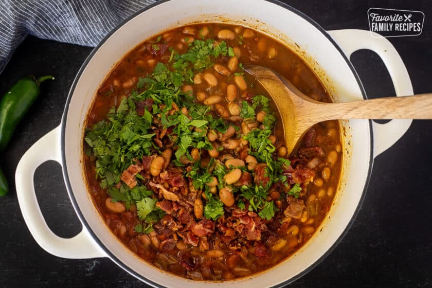 Stirring in bacon and cilantro into Charro Beans with a wooden spoon.