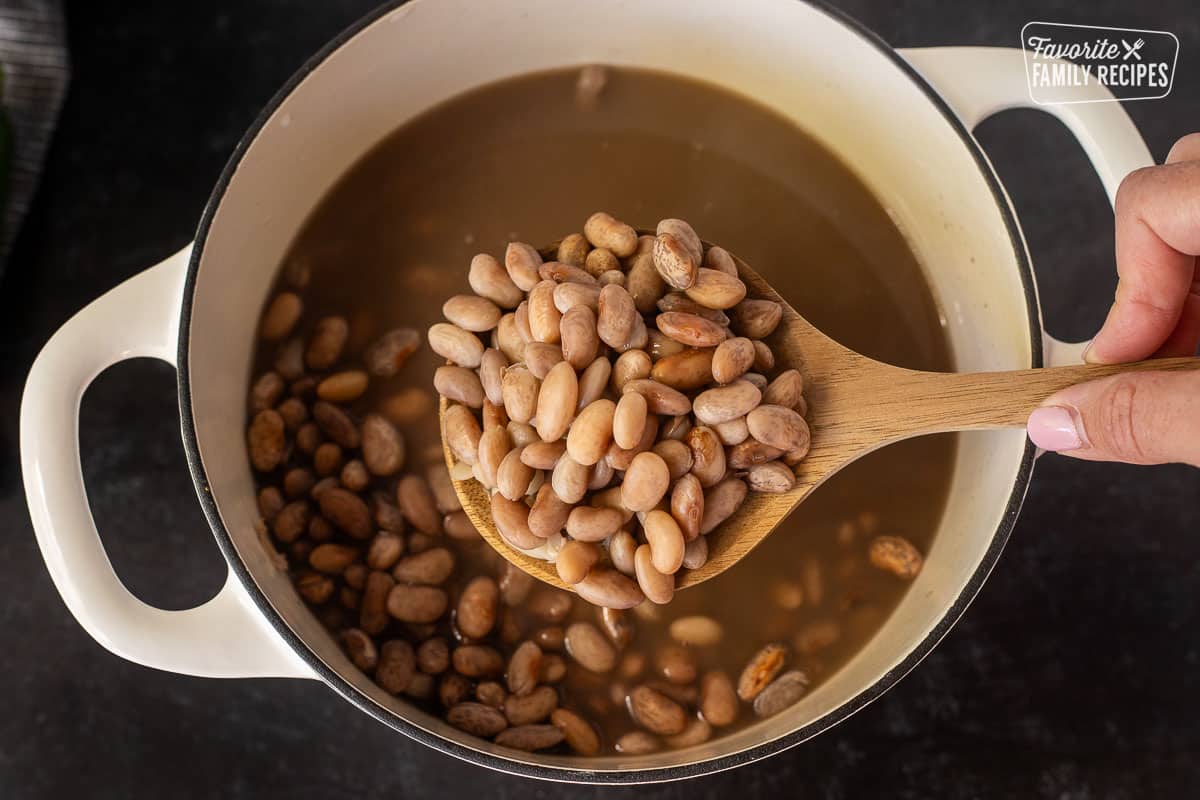 Soaked pinto beans in a wooden spoon holding over the dutch oven.