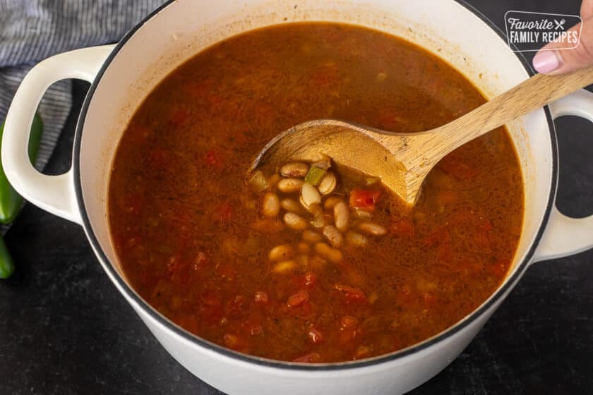 Stirring together Charro Bean ingredients with a wooden spoon in a dutch oven.