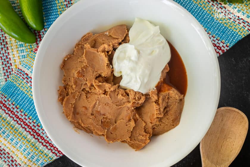 Glass mixing bowl with beans, sour cream and hot sauce. Wooden spoon on the side.