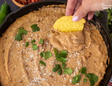 Chip dipping into skillet of Cheater Refried Beans topped with cojita cheese and cilantro.