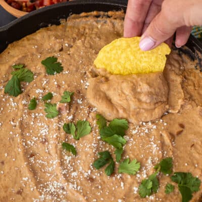 Chip dipping into skillet of Cheater Refried Beans topped with cojita cheese and cilantro.