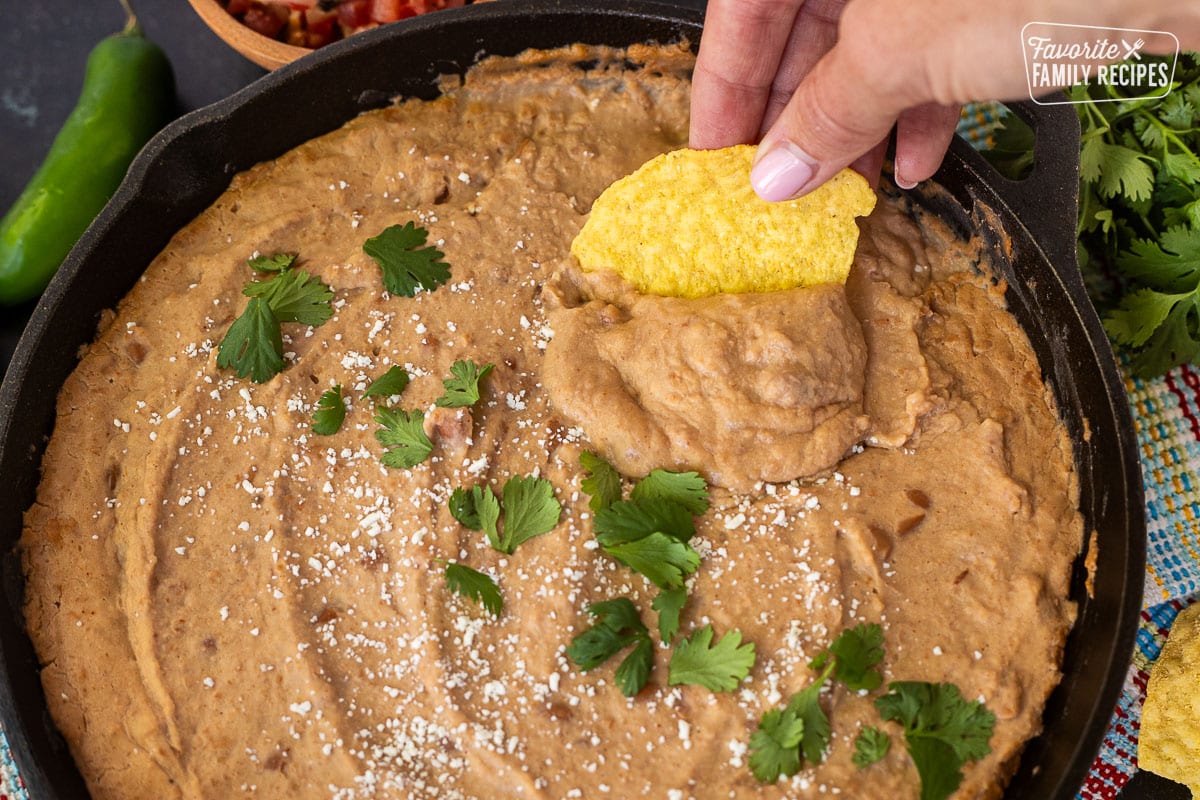 Chip dipping into skillet of Cheater Refried Beans topped with cojita cheese and cilantro.