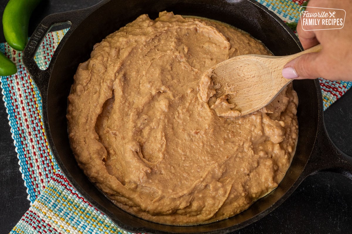 Smoothing refried beans into skillet with a wooden spoon.