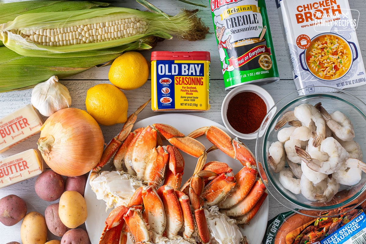 Ingredients to make Crab Boil including creole seasoning, chicken broth, Old Bay, lemons, corn on the cob, paprika, raw shrimp, beef smoked sausage, crab legs, potatoes, butter, onion and garlic.