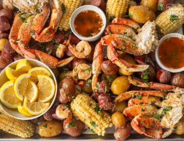 Sheet pan with crab legs, sausage, shrimp, corn, potatoes and lemon wedges.