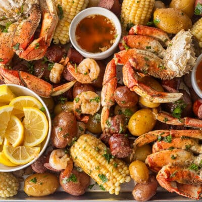 Sheet pan with crab legs, sausage, shrimp, corn, potatoes and lemon wedges.