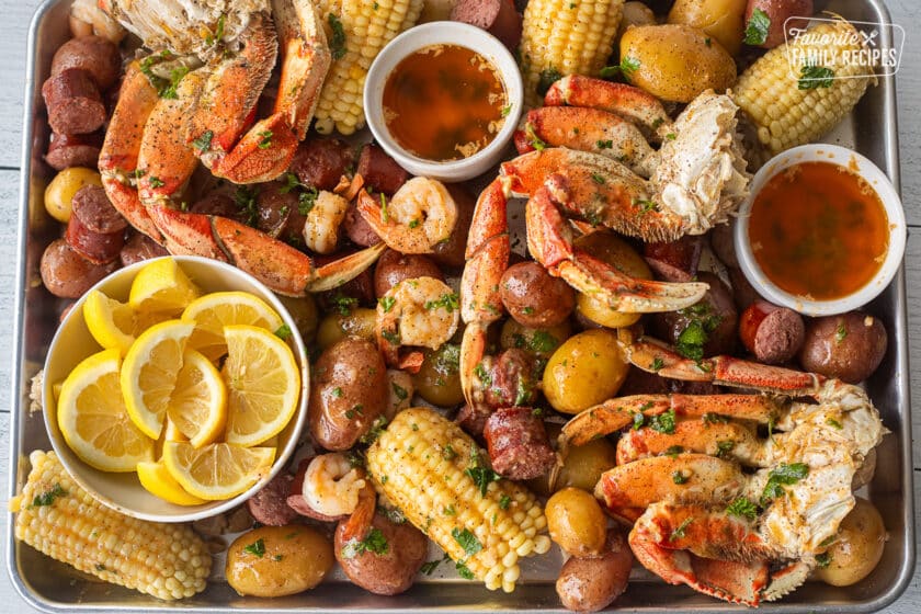 Sheet pan with crab legs, sausage, shrimp, corn, potatoes and lemon wedges.