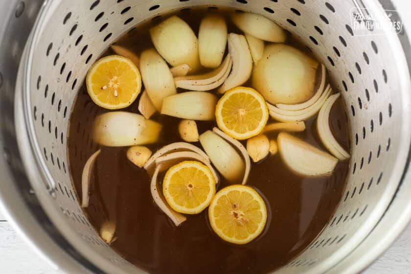 Stock pot with broth, seasonings, onion, garlic and lemon.