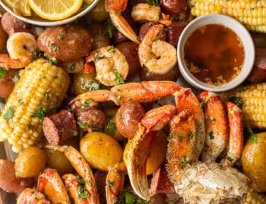 Sheet pan with crab legs, shrimp, potatoes, sausage, corn, butter and lemon wedges.