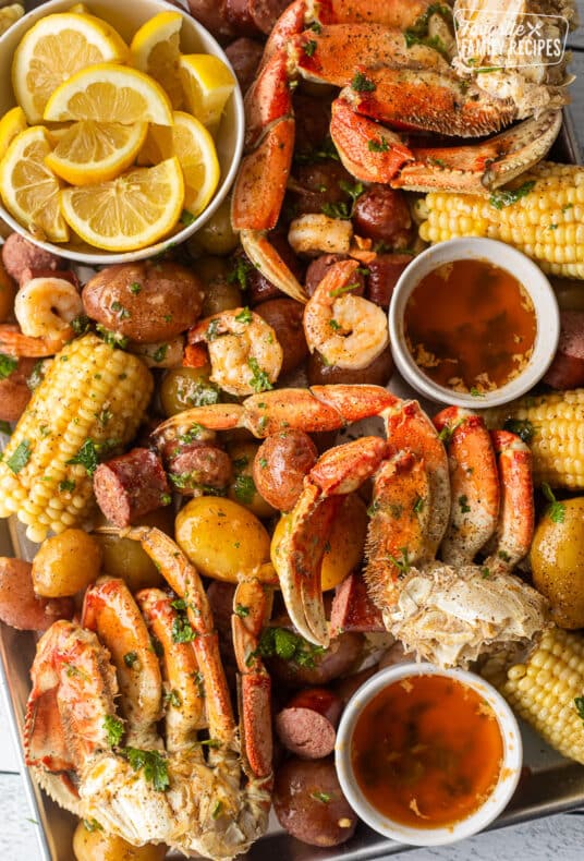 Sheet pan with crab legs, shrimp, potatoes, sausage, corn, butter and lemon wedges.
