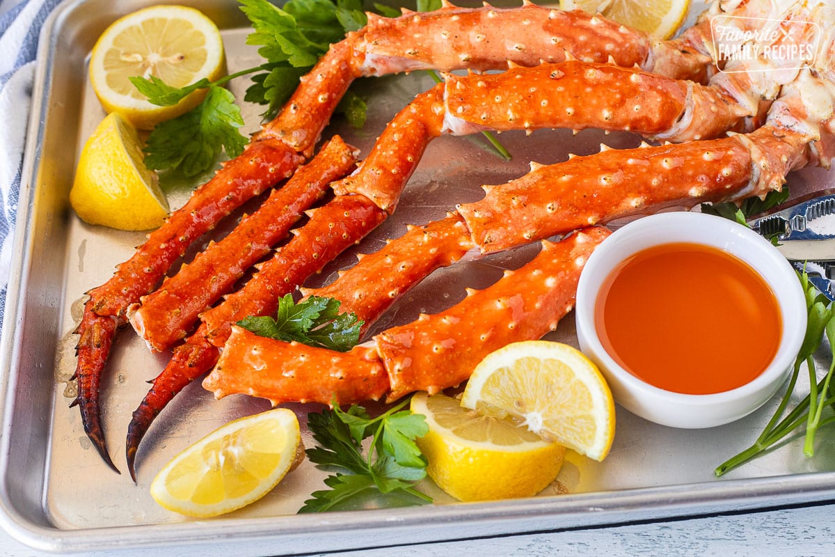 Baked crab legs on a sheet pan with butter, lemon wedges and parsley.