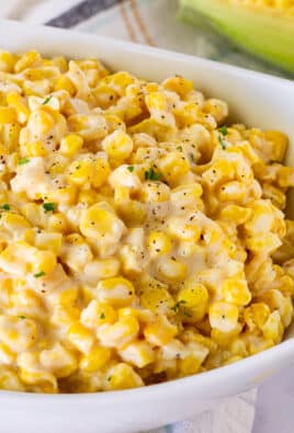 Bowl of Creamed Corn garnished with fresh parsley, salt and pepper. Fresh corn in the background.