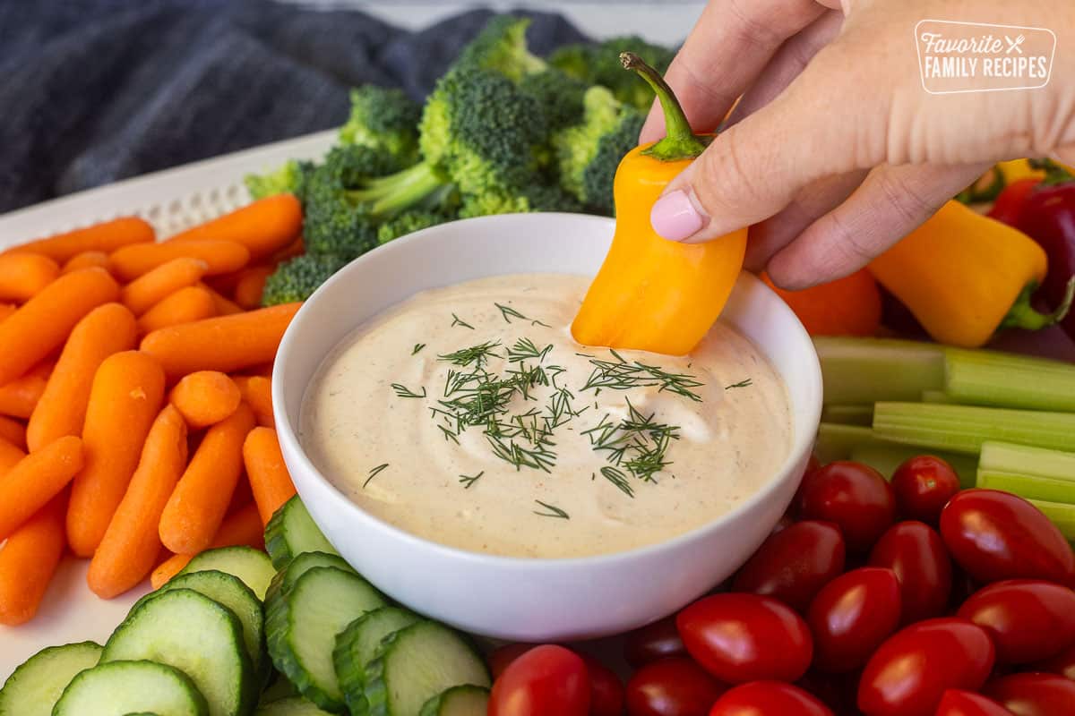 Dipping a yellow bell pepper into a bowl of veggie dip.