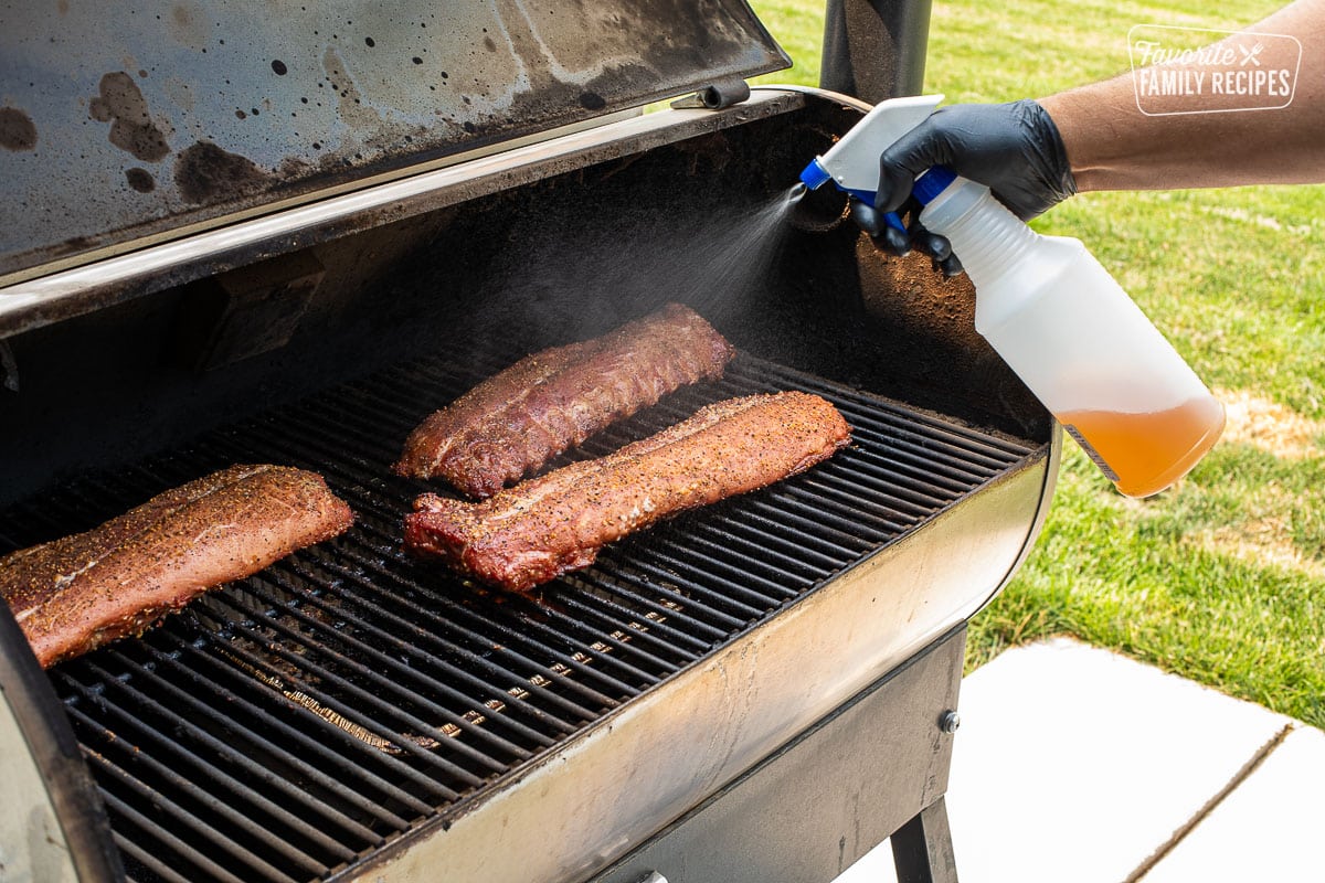 Spraying apple cider vinegar on racks of ribs in the smoker.