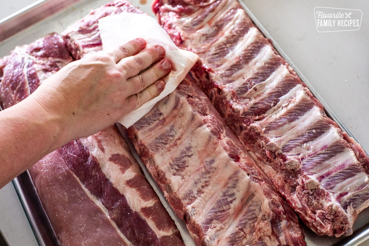 Patting down raw ribs with paper towels.