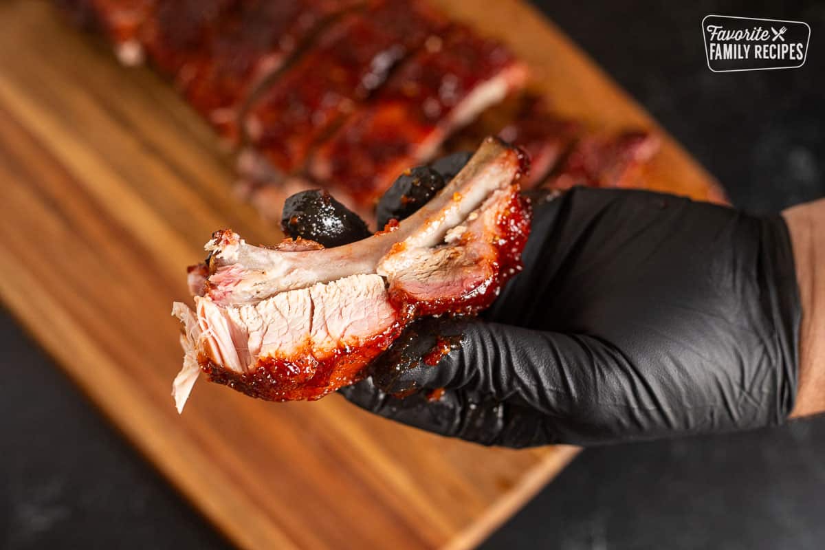 Hand holding a cut piece of smoked ribs.