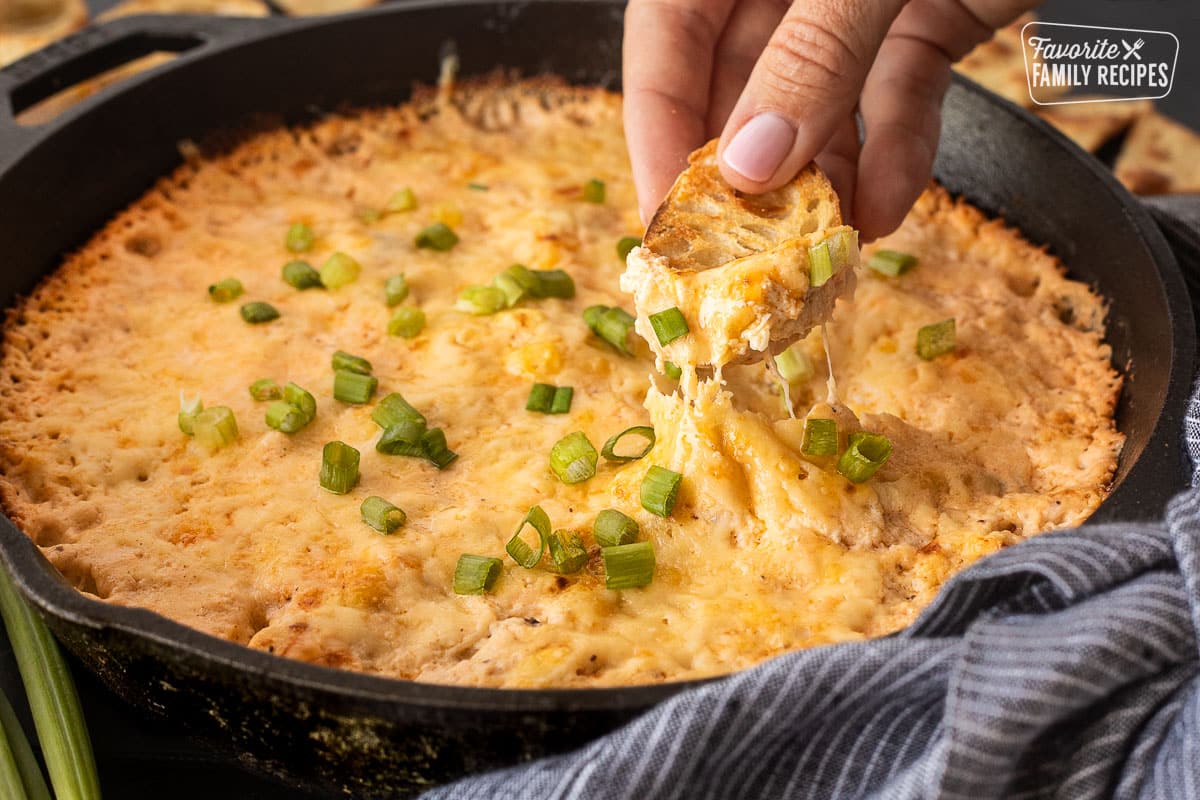 Dipping a slice of bread into a skillet of Hot Crab Dip.