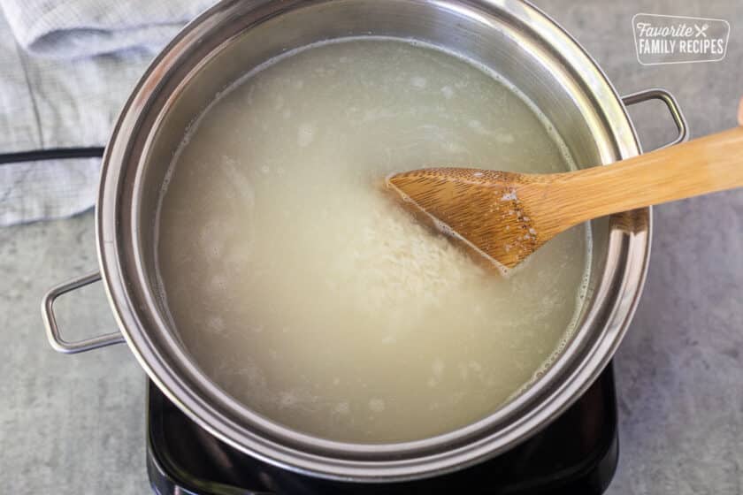 Stirring rice in a saucepan of boiling water with a wooden spoon.