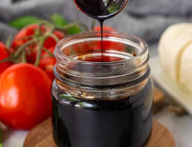 Jar of Balsamic Glaze and balsamic glaze drizzling from a wooden spoon.