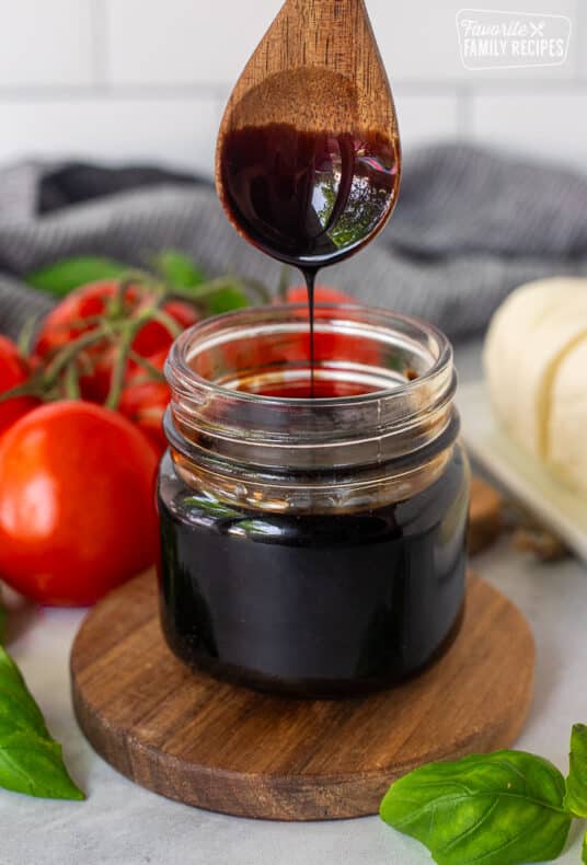 Jar of Balsamic Glaze and balsamic glaze drizzling from a wooden spoon.