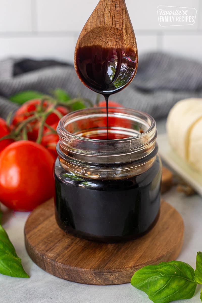 Jar of Balsamic Glaze and balsamic glaze drizzling from a wooden spoon.