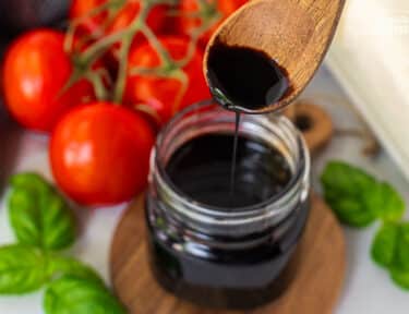 Jar of Balsamic Glaze and balsamic glaze drizzling from a wooden spoon.