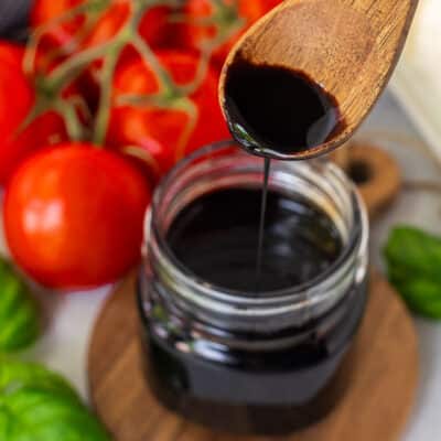 Jar of Balsamic Glaze and balsamic glaze drizzling from a wooden spoon.