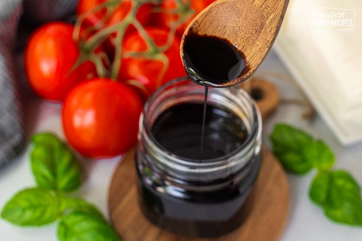 Jar of Balsamic Glaze and balsamic glaze drizzling from a wooden spoon.