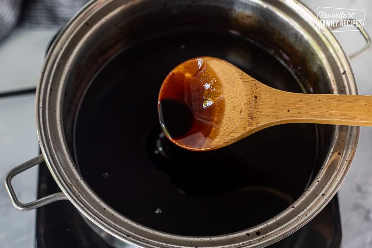 Wooden spoon holding up balsamic glaze from saucepan.