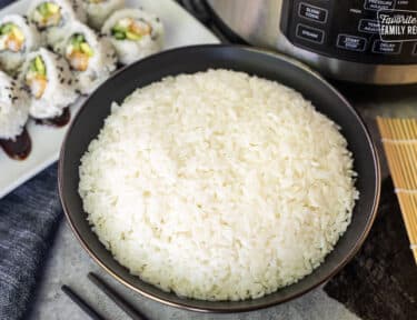 Bowl of Instant Pot Sushi Rice next to sushi roll and instant pot.