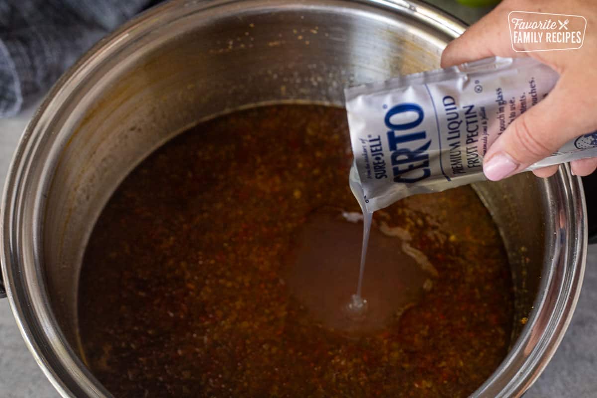 Pouring liquid pectin into pot of jalapeño pepper jelly.