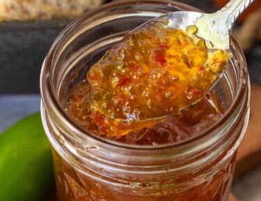 Spoon of Jalapeño pepper jelly coming out of a jar.