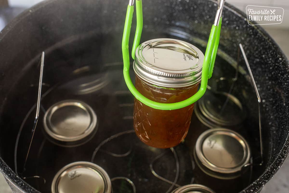 Lifting a canning jar with tongs out of a water bath.