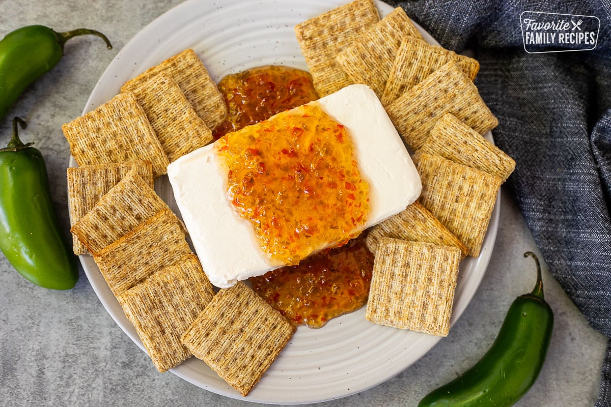 Plate with a block of cream cheese with jalapeño pepper jelly on top and surrounded by crackers.