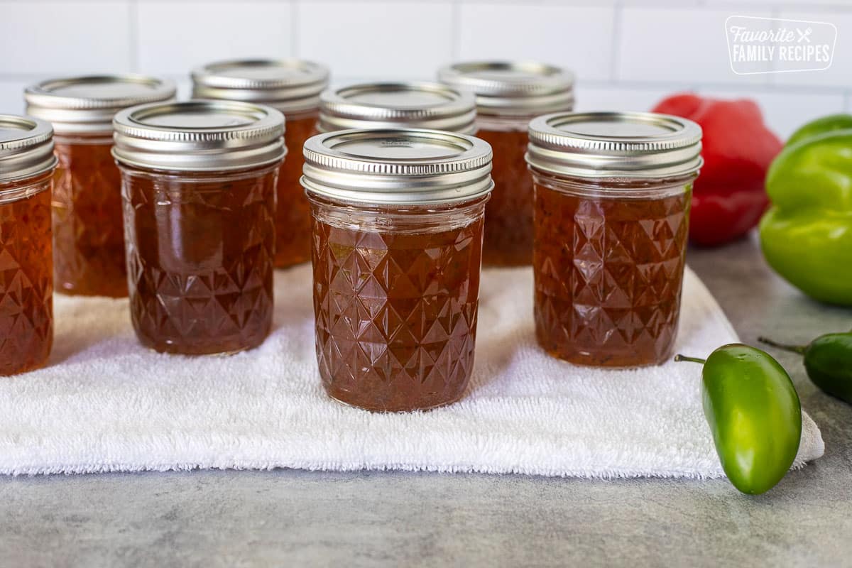 Hot canning jars of jalapeño pepper jelly resting on a towel.