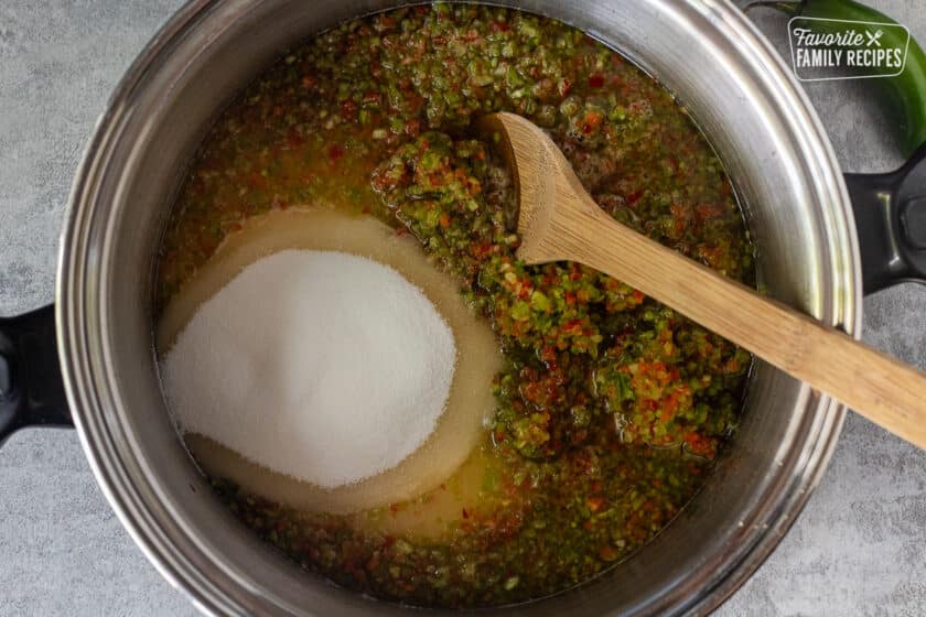 Large pot with ingredients to make jalapeño pepper jelly and wooden spoon.