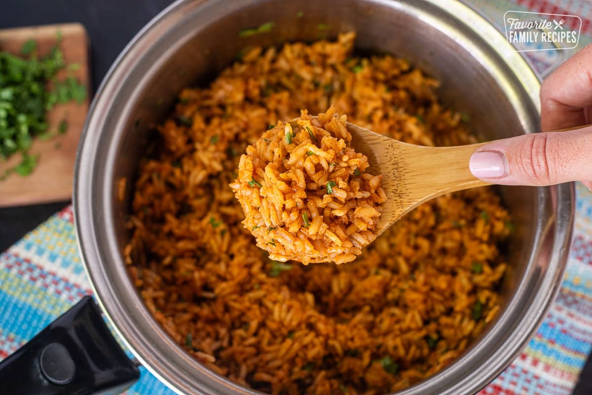 Wooden spoon with Mexican Rice held over a saucepan.