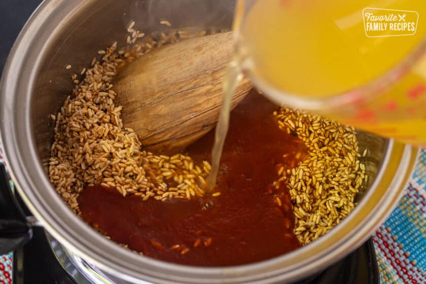 Pouring chicken broth into sauce pan with golden rice and tomato sauce for making Mexican rice.