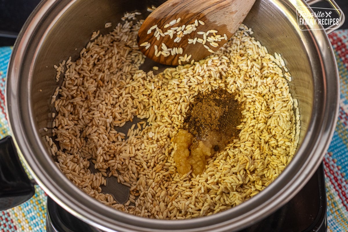 Garlic and seasoning added to golden cooked rice in a saucepan.