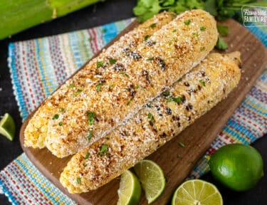 Three cobs of Mexican Street Corn next to fresh lime and cilantro.