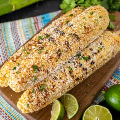 Three cobs of Mexican Street Corn next to fresh lime and cilantro.