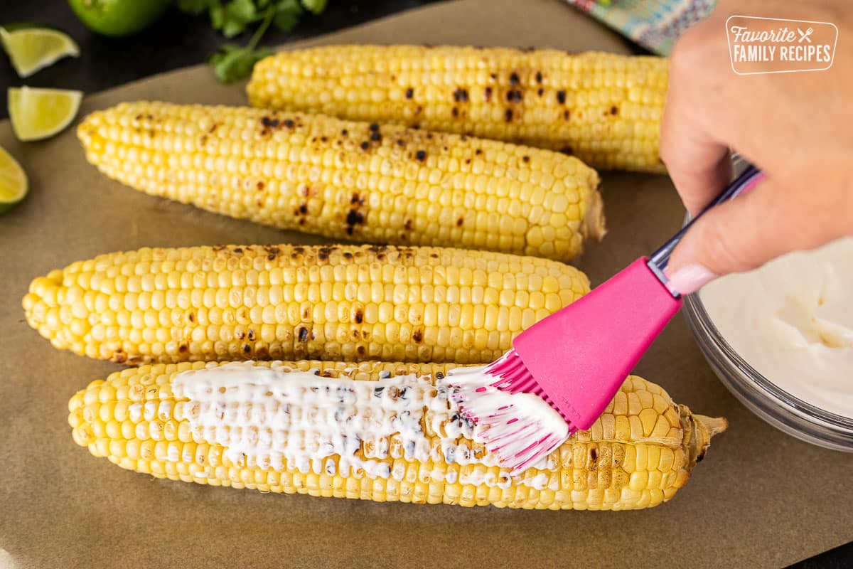 Brushing mayonnaise and sour cream mixture onto hot grilled corn.