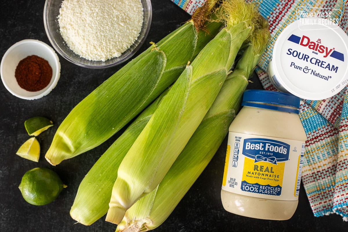 Ingredients to make Mexican Street Corn including corn on the cob, sour cream, mayonnaise, limes, chili powder and cojita cheese.