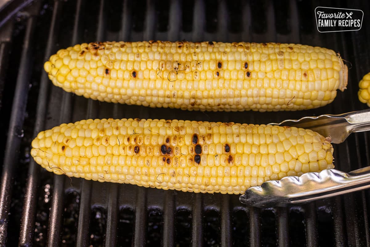 Grilling corn on the cob on barbecue with tongs.